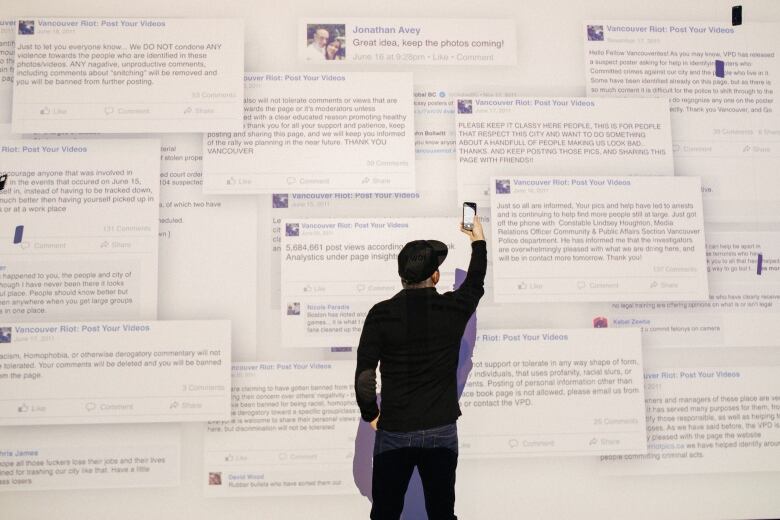 A man holds a phone camera up to a projected wall of Facebook comments.