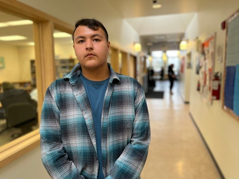 A young man in a plaid shirt stands in the hall of a school.