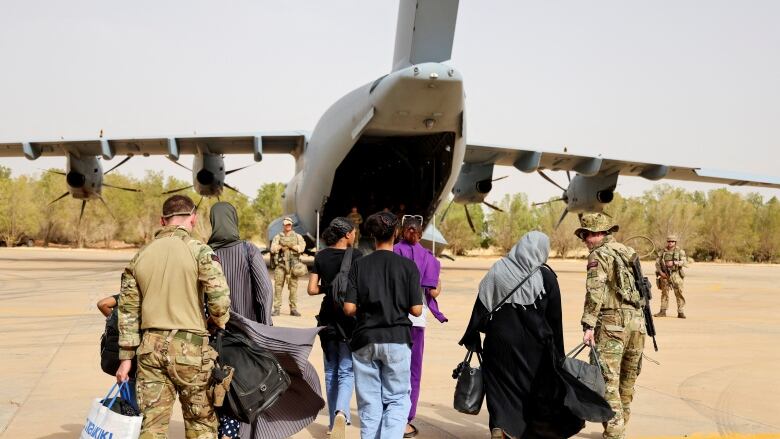 A group of people, some wearing military fatigues, walk towards a small plane.