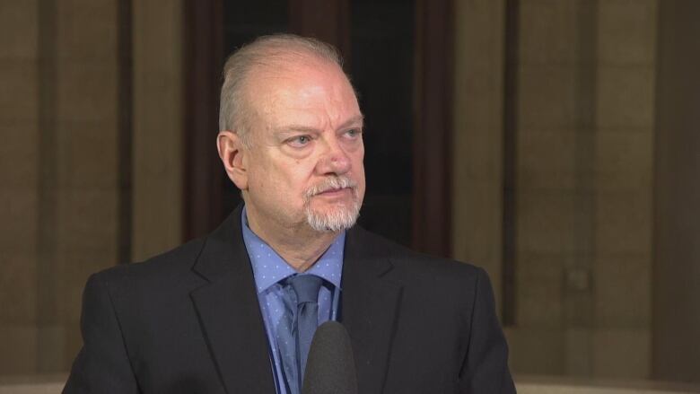 A politician in a dark blazer blue coat speaks into a microphone.