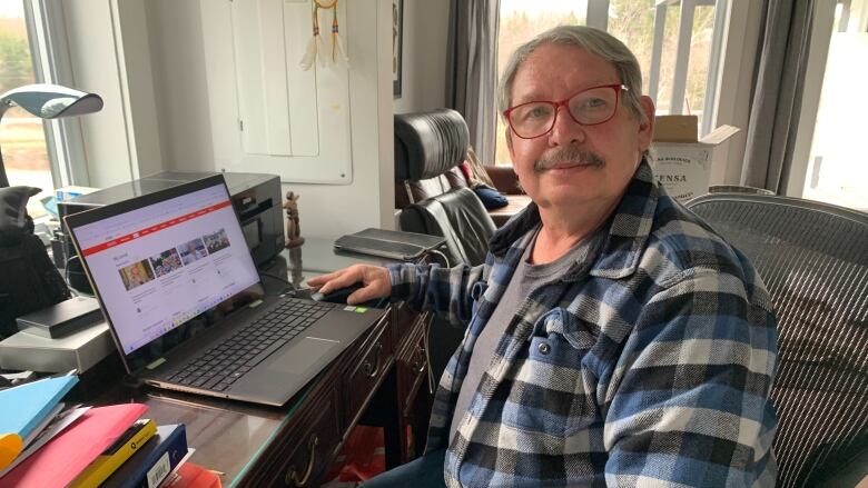 A man sits at a desk in front of a laptop.