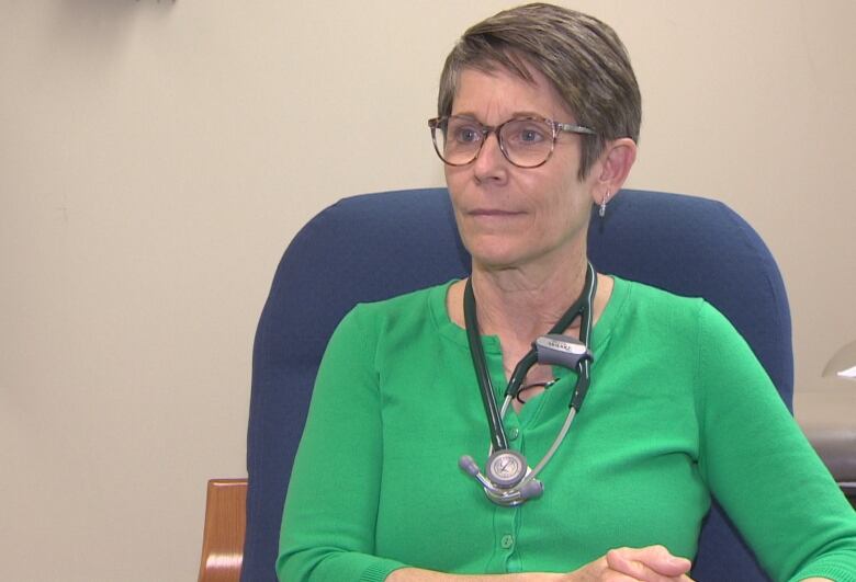 A woman with glasses sits in a chair.