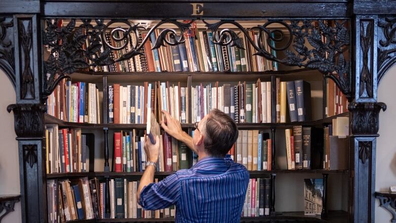 A man in a blue shirt pulls a book from a bookshelf. The bookshelf is framed by dark brown wood and a yellow letter E.