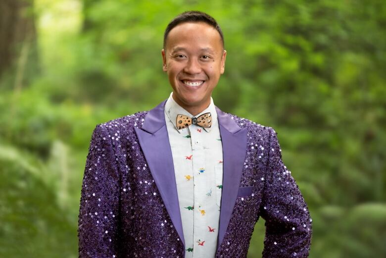 A man with short brown hair wears a glittery purple blazer and orange bowtie. 