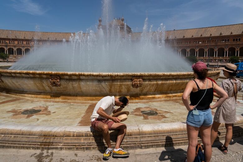 A man sits near a public fountain on a hot day.