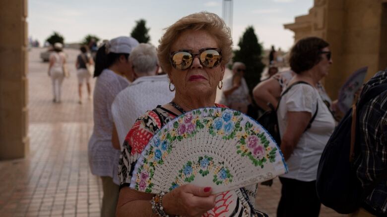 A woman cools herself with a fan.