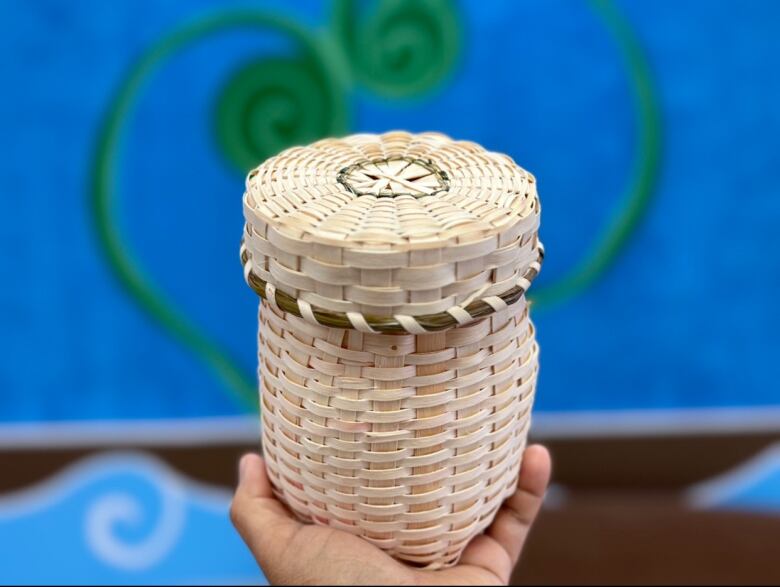 A small basket made of light, woven wood sits in the palm of a hand.