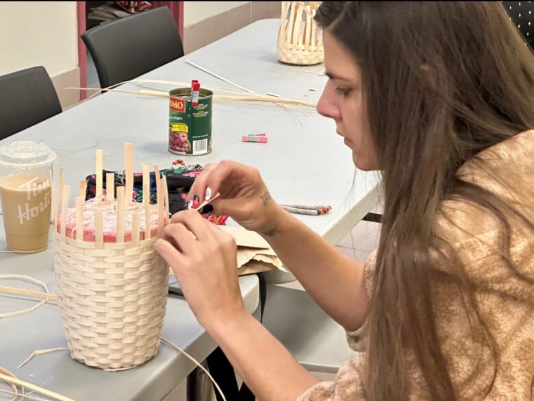 A woman sits at a table weaving a basket.