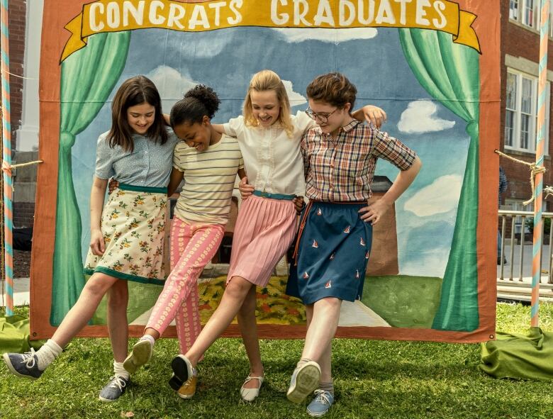 Four preteen girls dance in front of a painted sign.