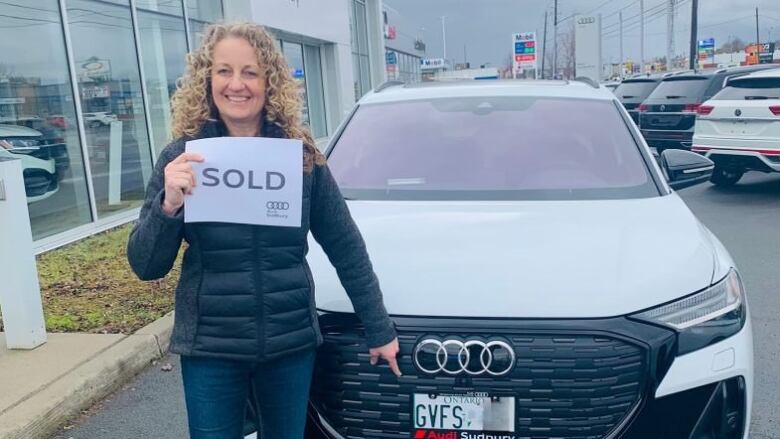 A woman with curly hair holding a sold sign while standing in front of an SUV.