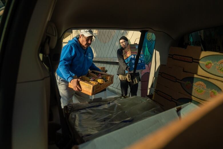 A man and woman put a box of pineapples into the back of a van 