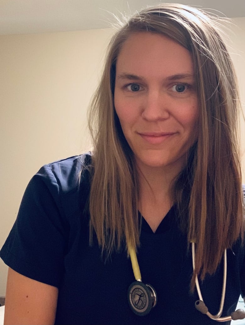 A nurse, in dark blue scrubs with a stethoscope, looks at the camera.