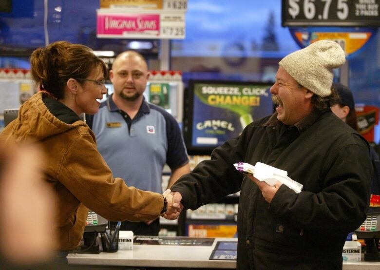 A woman and a man shake hands inside a store.