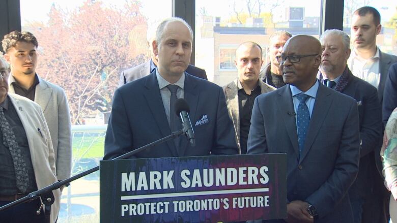 Two men standing a podium with a group of people in the background.