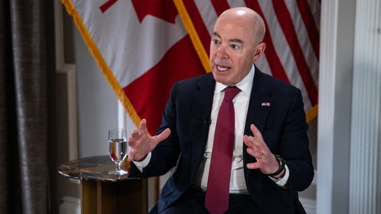 A man in a dark suit and red tie answers a question during an interview.