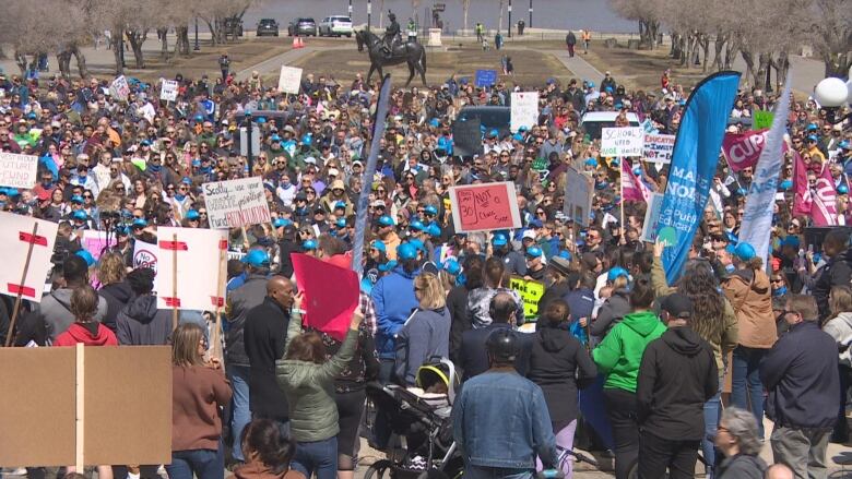 A large crowd of people, some carrying signs, stands outside.