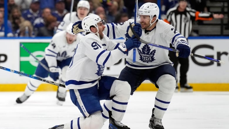 A male ice hockey player shouts in celebration while a teammate wraps his arms around him.