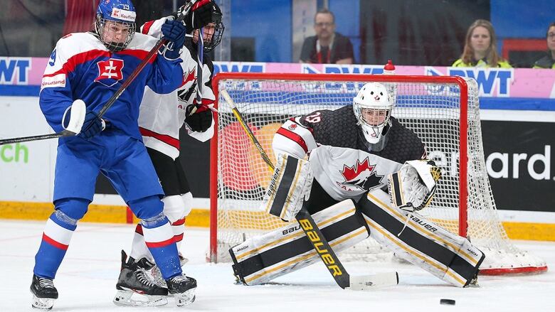 Men's goalie eyes a shot along the ice towards the net during an under-18 world hockey championship game.