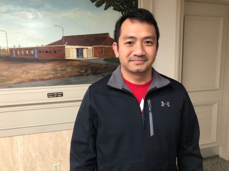 A man with black hair wearing a red t-shirt and a black sweater