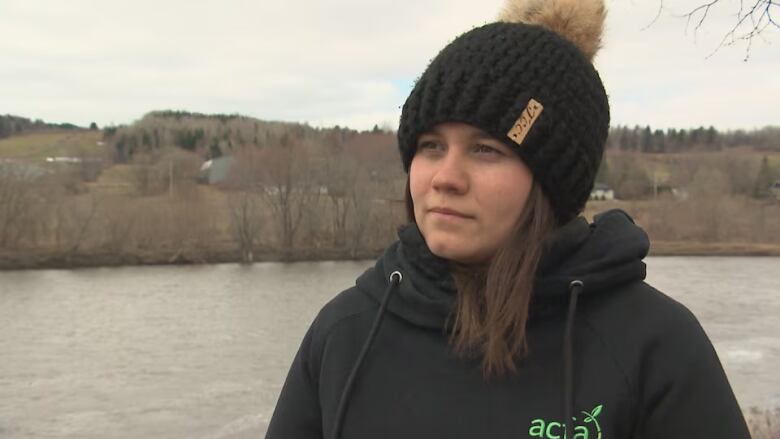 A woman wearing a black hoodie and toque stands outside.