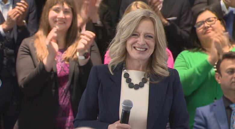 A woman holds a microphone standing in front of a crowd.