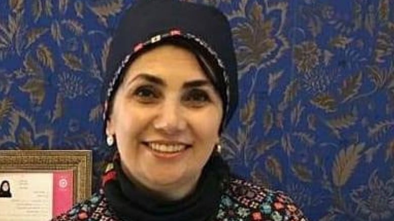 A portrait of a smiling woman wearing a navy scarf on her head and a multi-colour blouse.