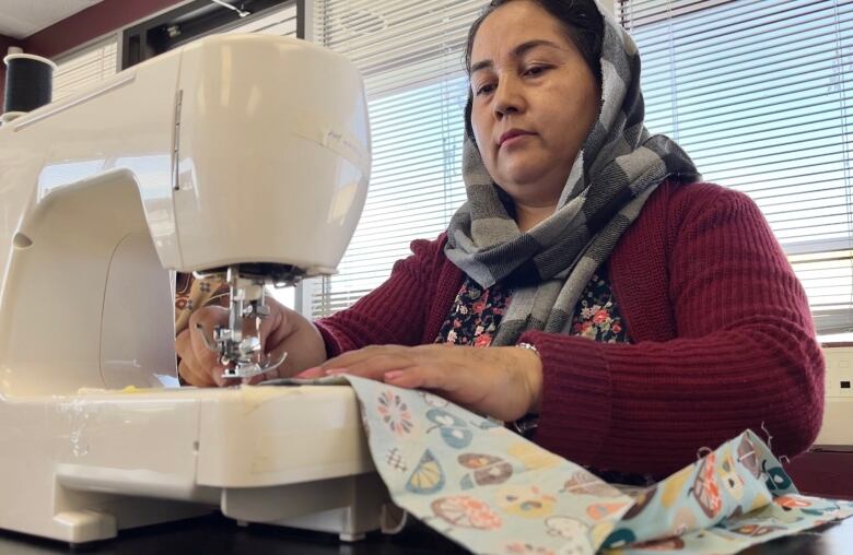 A woman sits behind a sewing machine, stitching a piece of fabric. 