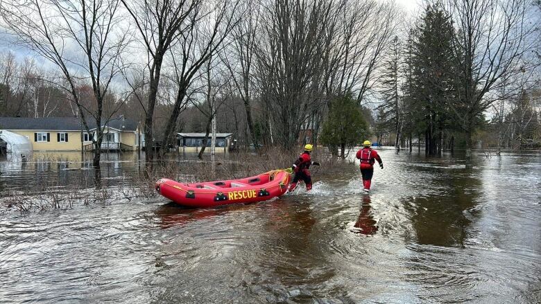 two firefighters wading through water with boat