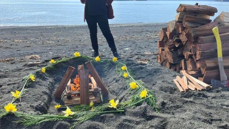 A fire with a ring of flowers and grass is pictured on a beach.