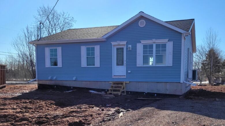 A small blue bungalow with no front porch and no landscaping yet.