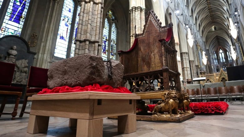 A large stone sits on a platform in front of a medieval chair inside a large abbey.