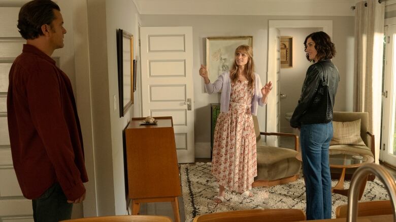 A man and two women stand in a living room.