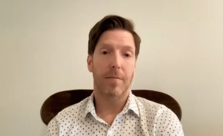 Man in a collared shirt sitting in front of a blank beige wall