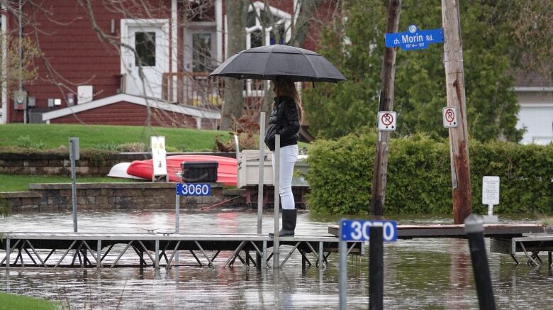 A woman stands on a temporary bridge over a road as water levels rise.