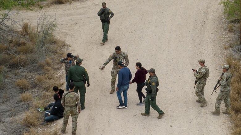 Individuals interspersed with people in camo military gear holding weapons.