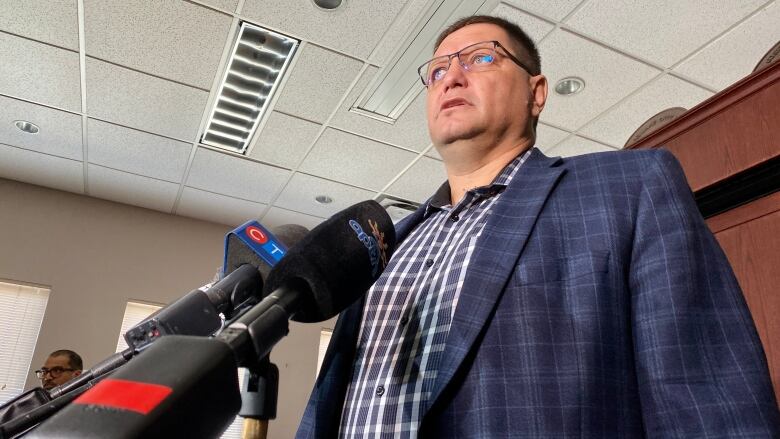 A man in a blue suit speaks into news outlet microphones. 