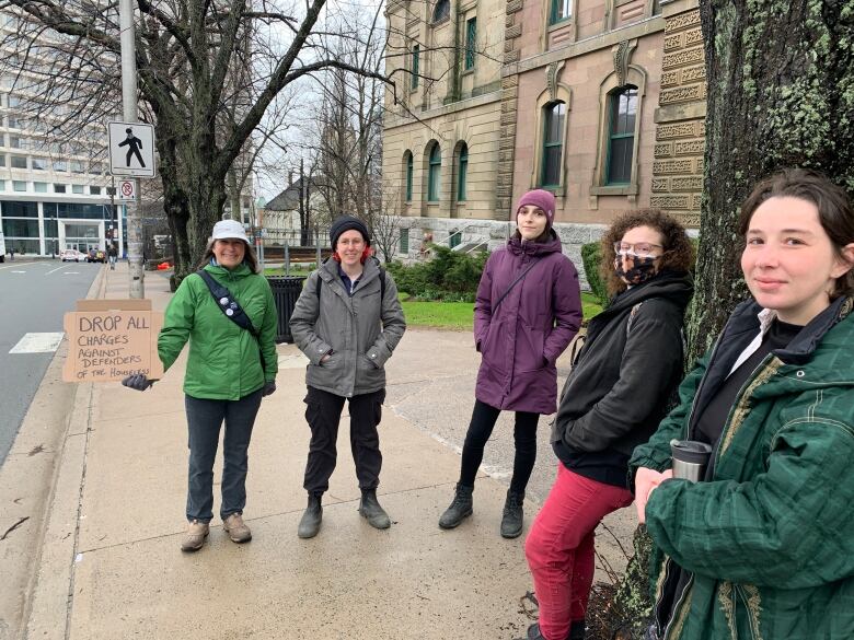 Five people stand on a downtown Halifax street. One holds a cardboard sign reading 