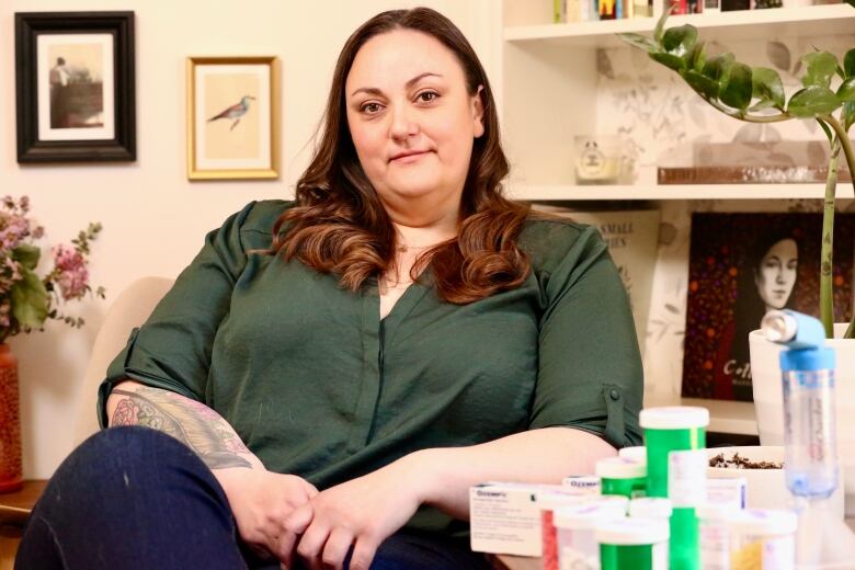 Emma Cloney wearing a green shirt, sits at home with several medications for Lipedema in front of her.