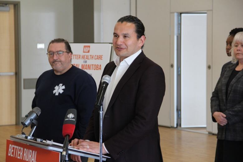 A man speaks behind a podium, equipped with microphones. 