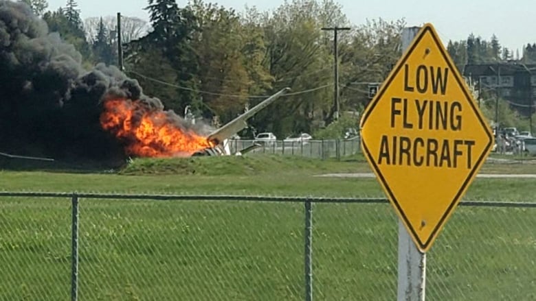 A plane is seen on fire next to a sign that reads 'Low flying aircraft'.