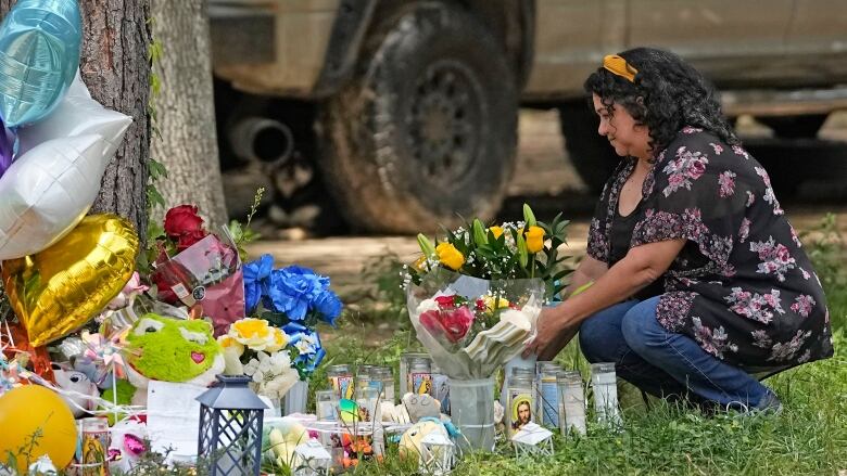 A woman squats down beside a memorial of flowers and stuffed animals 