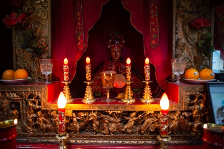 A statue is pictured surrounded by candles and intricate carvings. 