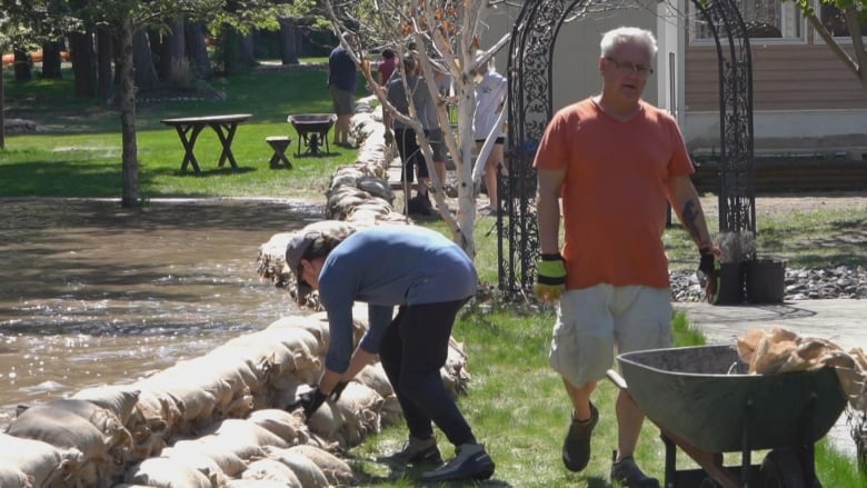 A man walks away from a wall of sandbags as pooled water is seen in a grassy area next to homes.