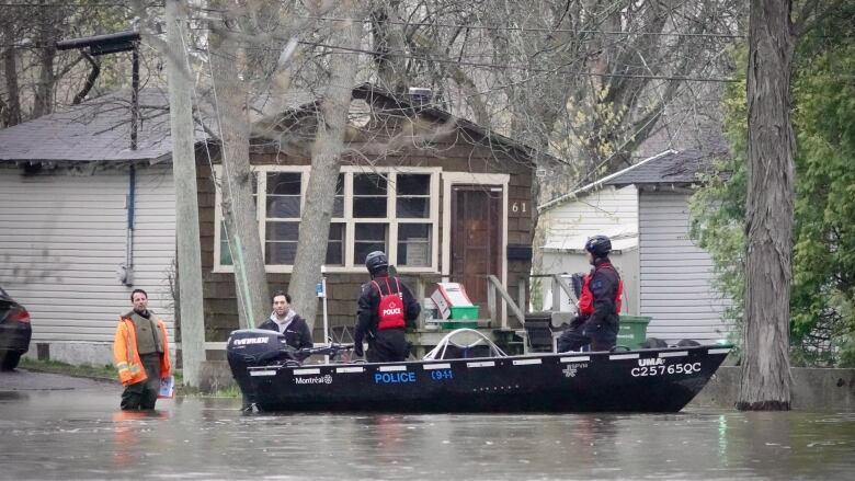 Two men standing in water look at police officers in a boat. 