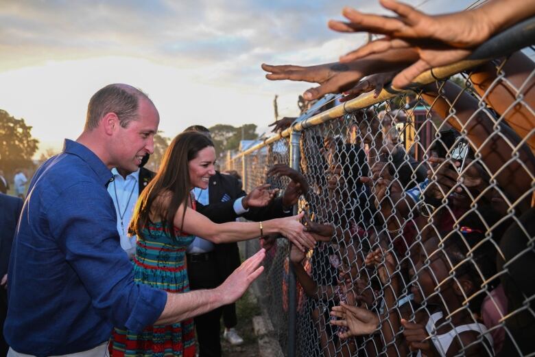 Two people greet a crowd reaching out through a chainlink fence.