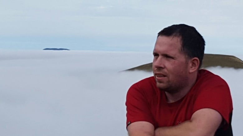 A man looks out with clouds behind him