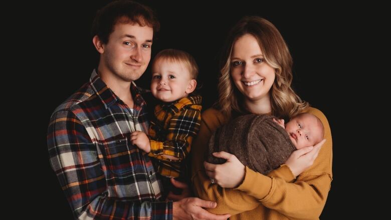 A family of four poses for a photo in front of a black backdrop.