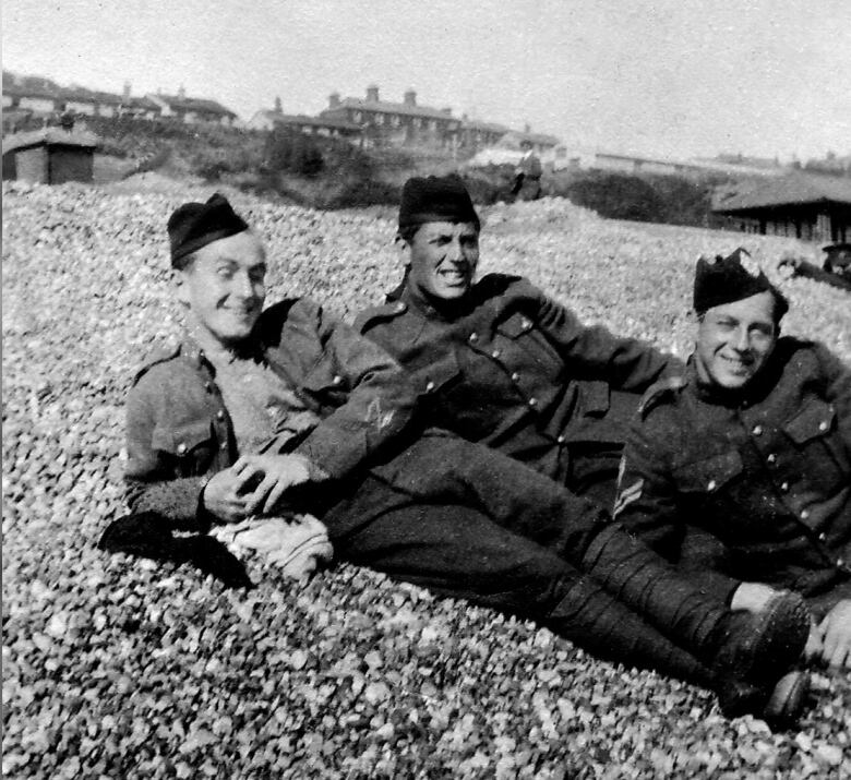 Three soldiers in uniform are pictured lying on a rocky ground smiling at the camera in a black and white archive photo.