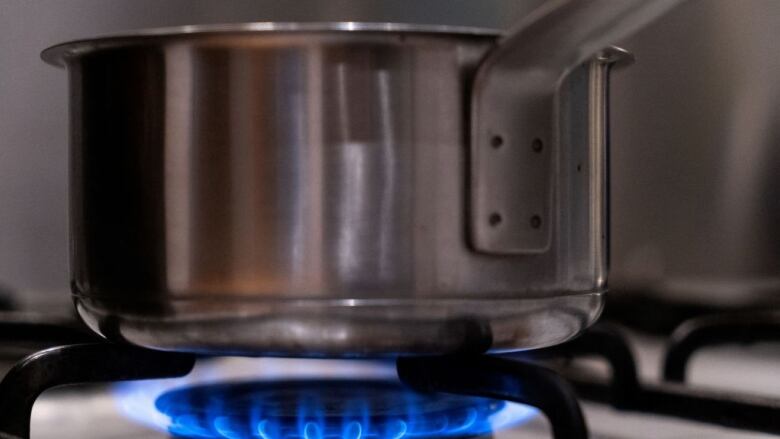 A metal pot sits over the blue flame of a gas stove.