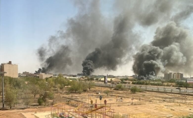 Smoke from fires and explosions rises from the ground in the distance of a war-torn city.